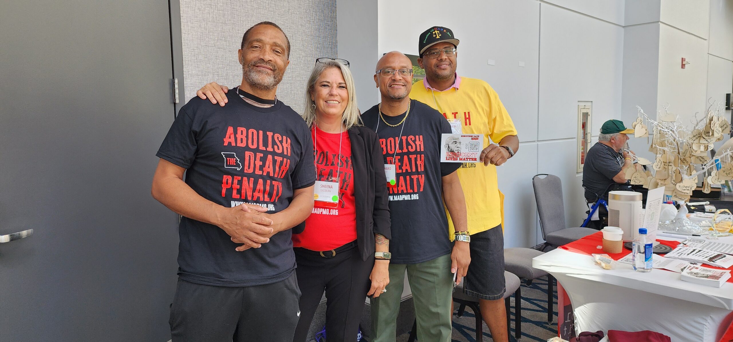 Three People Stand Beside a Table, Smiling Together.